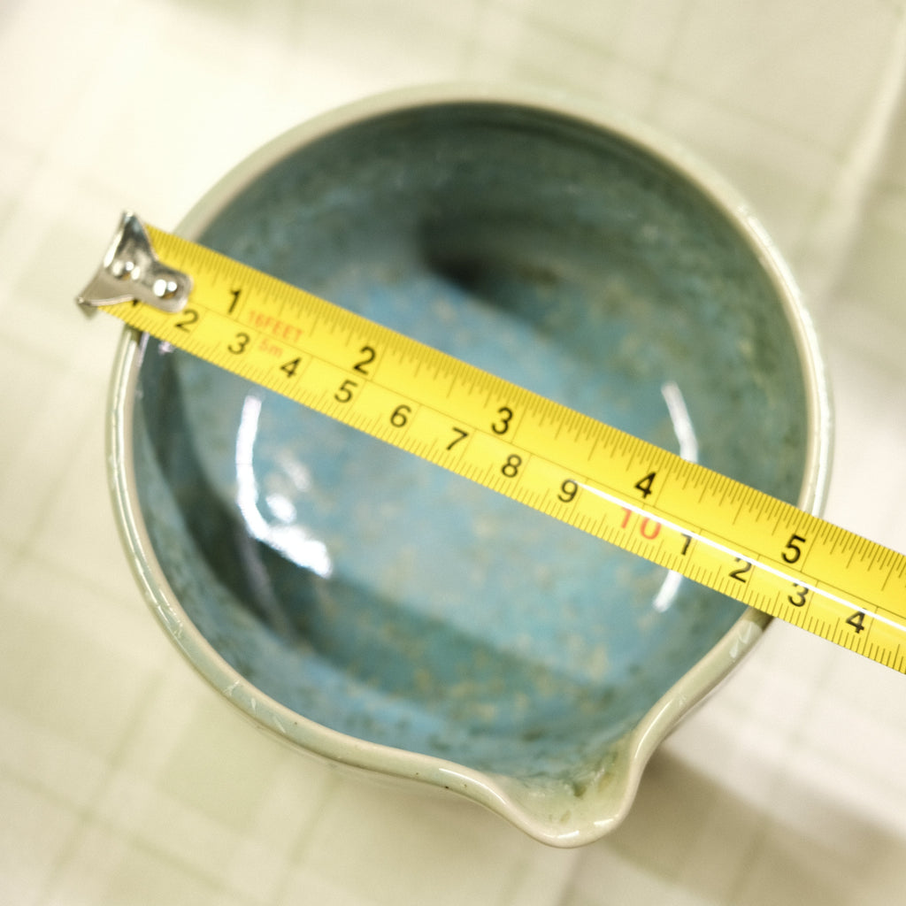 Ceramic bowl with a measuring tape indicating its dimensions on a textured surface